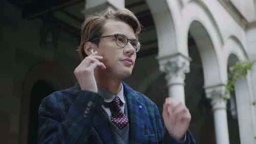 Closeup Serious Student Putting on Wireless Earphones at University Territory. Young Man