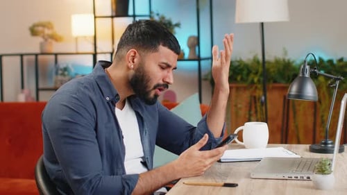 Indian Man Using Smartphone Browsing Loses Bad News Fortune Loss Fail at Home Office Desk Workplace