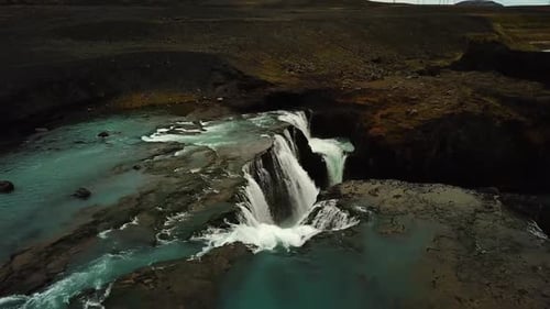Aerial drone view over river water flowing down a large waterfall, in Iceland