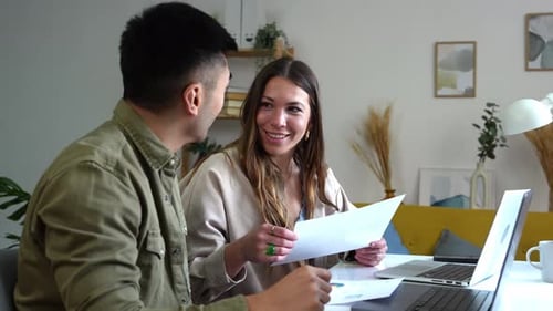 Couple Reviewing Data on Laptop and Paper Documents