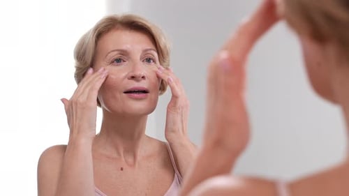 Woman Applies Facial Cream in Bright Mirror