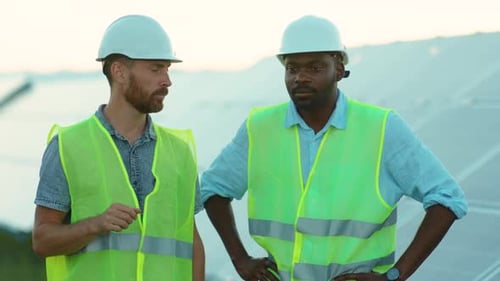 Porträt Afroamerikanische und kaukasische Ingenieure stehen in Sonderuniform auf dem Solarpark Diskutieren