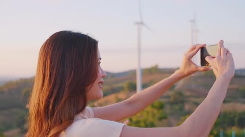 Asian woman using phone taking a photo outdoors in the wind turbine field.