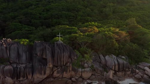 A giant Christian cross on top of a huge granite boulder in La Digue, Seychelles, bathed in gorgeous