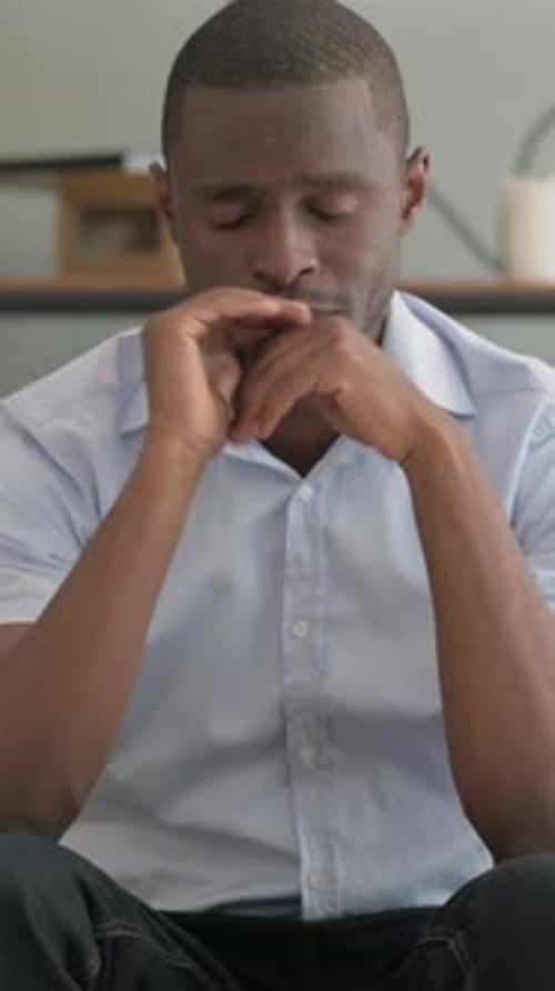 Worried Man Sits Inside With Hands Clasped