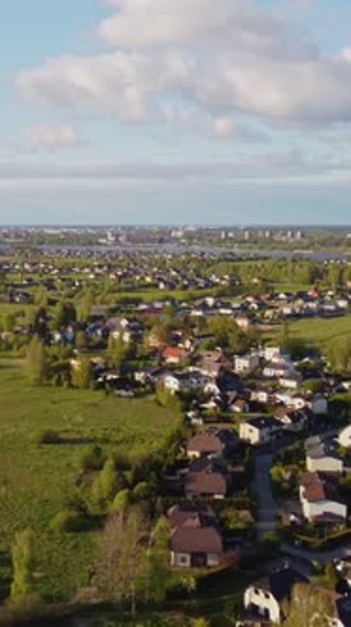 ertical slow drone pull out revealing Katlakalns residential area expanding toward Riga skyline