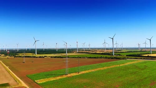 Agricultural field with wind mills and electricity power lines. Sustainable energy concept.