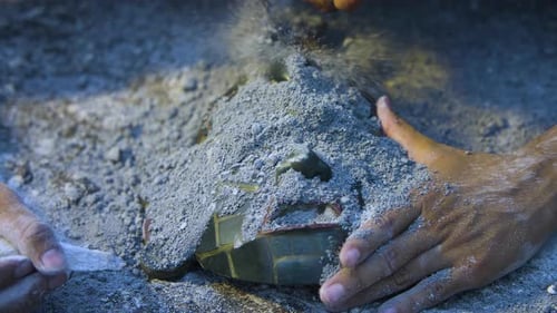 Hands Uncover Ancient Mask Covered in Ash