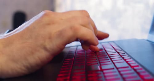 Fingers Typing on Red Backlit Laptop Keyboard