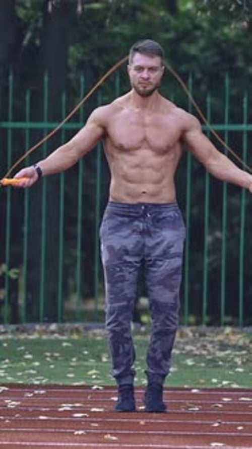 Fit man jumping rope on stadium. Male athlete performs exercise jump on rope on stadium