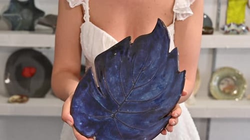 Woman in white dress showing a blue plate, final result at pottery workshop