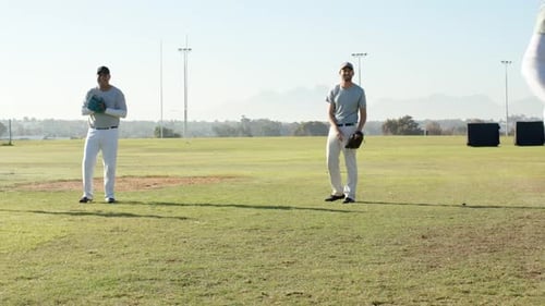 Diverse male teammates starting warm-up drill by catching and returning ball on field, with gloves