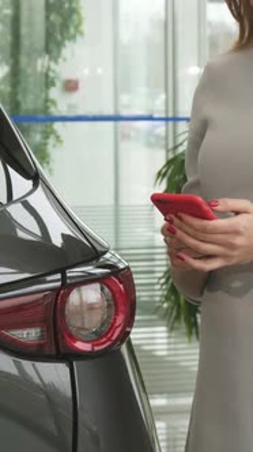 Chic Woman Engrossed in Smartphone at a Sleek Car Dealership