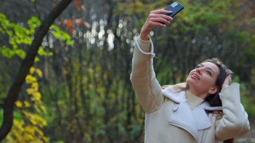Positive happy brunette taking selfie walking by the autumn park.