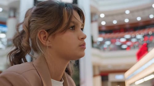 Young Woman Pausing in Mall Atrium Profile View with Soft Bokeh Lights Contemplative Expression and