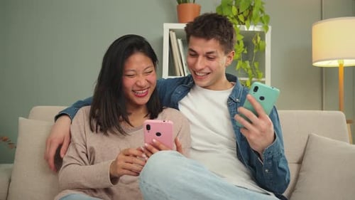 Smiling Couple Relaxing on Sofa with Mobile Phones