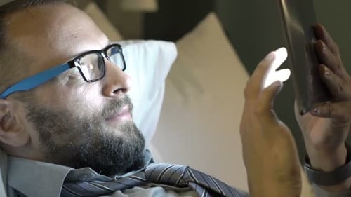 Young Businessman Working with Tablet Lying on Bed in Hotel Room At