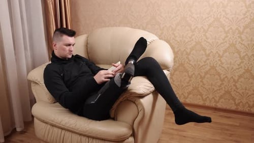 Young Adult Adjusting Athletic Prosthetic Leg in Chair