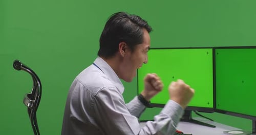 Happy Asian Man Celebrating While Working With Mock Up Multiple Computer Monitor In Green Screen