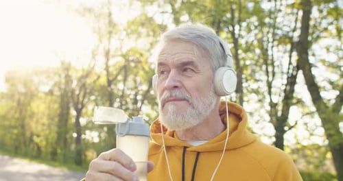 Close Up Portrait of Caucasian Handsome Senior Male Standing Outdoors Drinking Water From Bottle