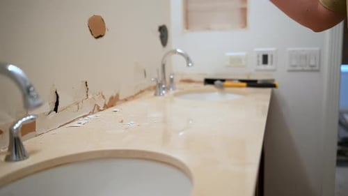 Construction Worker Using a Hammer to Break and Remove Bathroom Countertop Around Sink Area During
