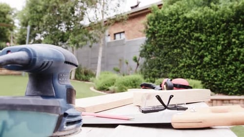Camera pushing ahead sander blurring while saw boards safety gear sitting on yard bench, copy space