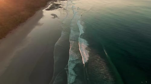 Drone flight along exotic Costa Rica beach with breaking tidal waves in sunrise