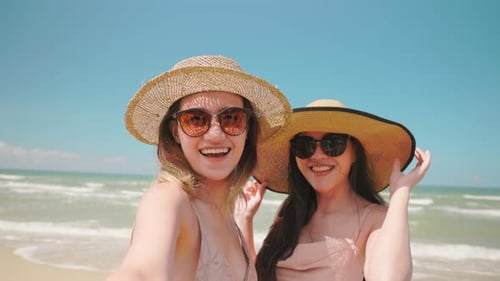 Two woman taking selfie video at beach with a smartphone on summer day