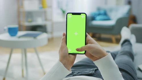 Woman at Home Lying on a Couch using Smartphone with Green Mock-up Screen, Doing Swiping, Scrolling
