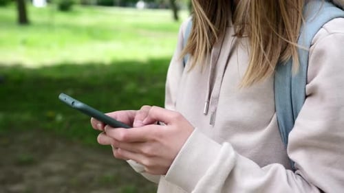 Little Shcoolgirl Typing Text On Her Smartphone In Park