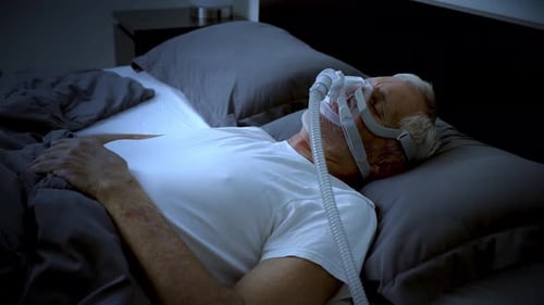 Mature adult sleeping at night while wearing a CPAP mask to treat his Sleep Apnea.
