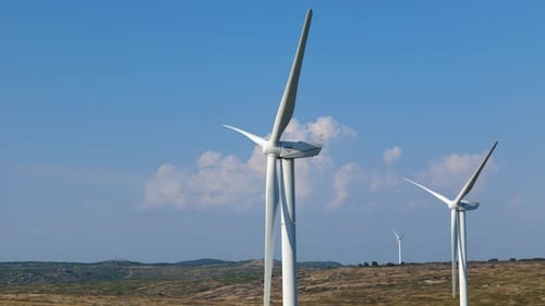 Slow establishing shot of windmills static with blue skies behind
