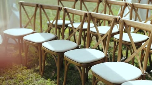 Dolly Shot of Wooden Chairs with White Pillows on It Closeup Outside Wedding Ceremony in Park Among