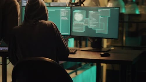 Hooded Figures Hacking Computers in Dark Room