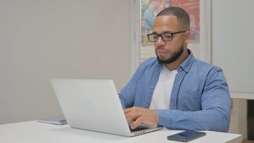 African Businessman Looking at Camera while Working on Laptop in Office