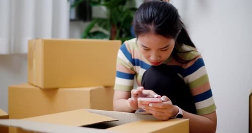 Woman Using Phone with Cardboard Boxes Indoors