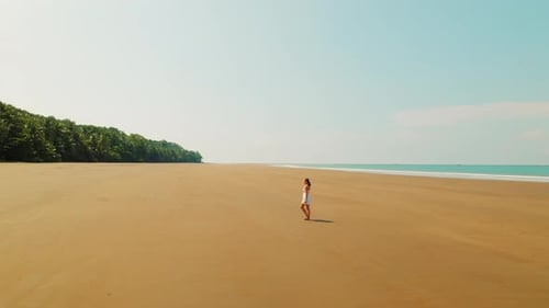 Woman in white dress walks across vast empty sandy beach in tropical Costa Rica