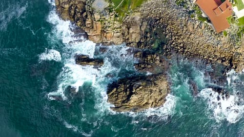 Top aerial drone view of waves crashing on rocky coastline. Blue ocean.