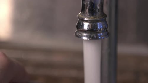 Water Flowing Out Of The Water Tap Into The Kitchen Sink. - close up shot