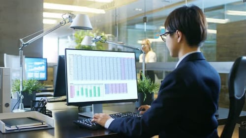 In the Office Businessman Works on the Personal Computer with Spreadsheets, Charts and Statistics.