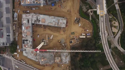 Vista desde un Zumbido orientado hacia abajo de un gran sitio de construcción con una gran grúa moviéndose debajo.