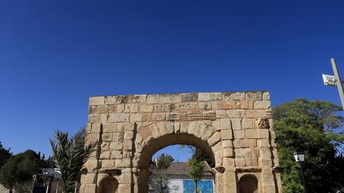 Journée ensoleillée mettant en valeur les ruines de l'ancienne arche romaine de Dougga, fond de ciel bleu clair, prise de vue fixe