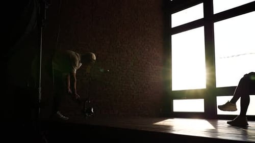 Man Adjusts Camera in Sunny Brick Walled Studio