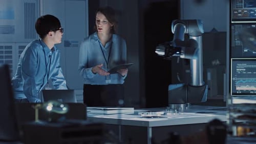 Man and Woman Engineers with Laptop and a Tablet Analyse and Discuss How a Futuristic Robotic Arm W