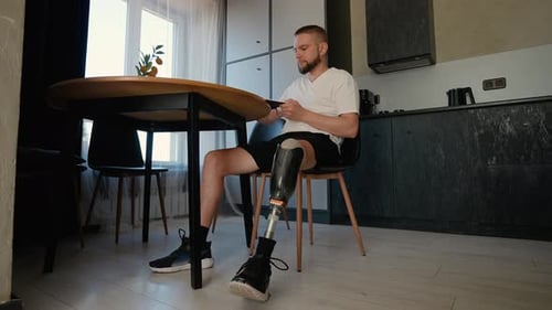 A Man with a Prosthetic Leg Sits at a Table Reading a Book During His Rehabilitation Process