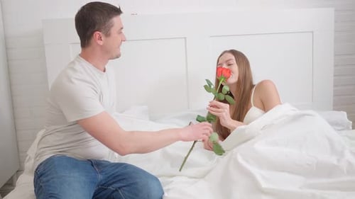 Romantic Couple Exchanging Gifts and a Rose in Bed