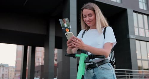 Woman Uses Smartphone with Teal Scooter in City