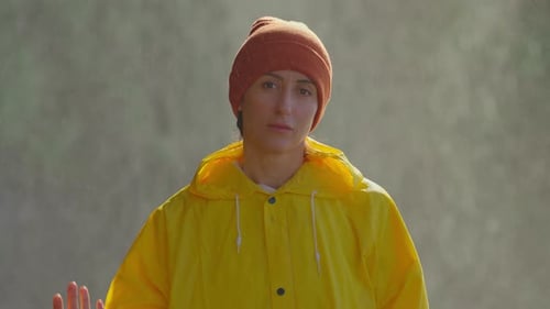 Woman Wearing Yellow Raincoat Puts on Backpack
