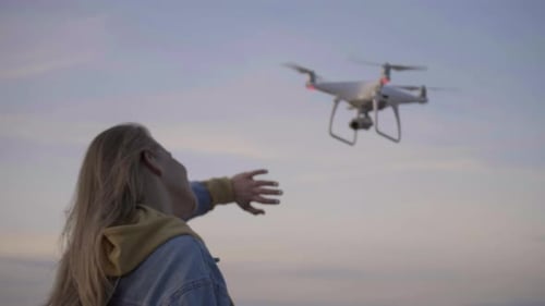 Junge Frau genießt Sonnenuntergang an der Küste, fliegt Drohne über Meer, Handgeste, Freiheit