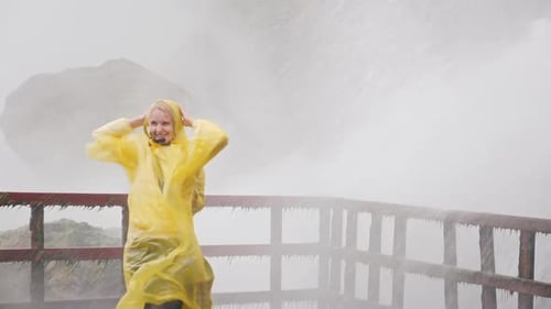 Woman in Yellow Raincoat Enjoying Misty Waterfall